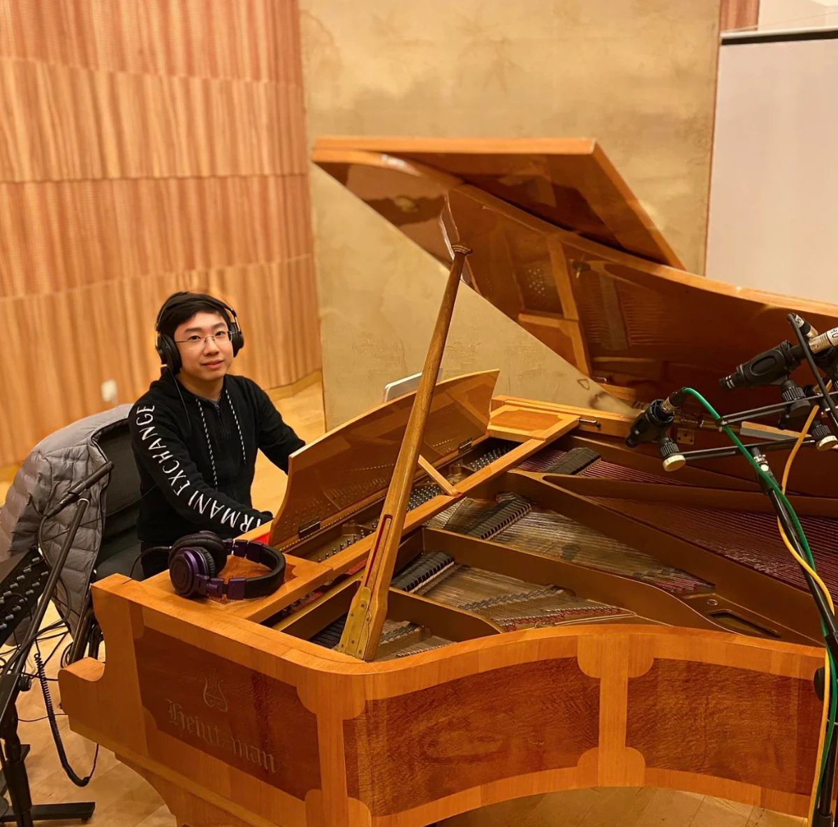 Xiao Huang seated at a grand piano in a recording room.
